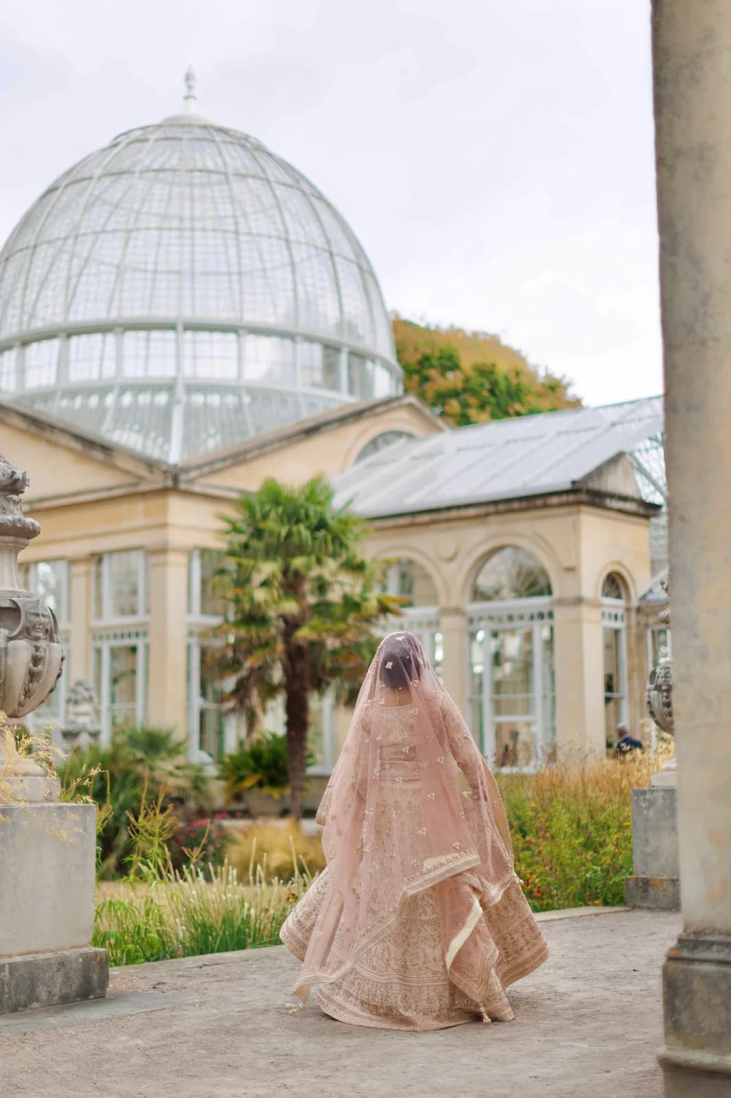A bride walking through a garden beside a glasshouse